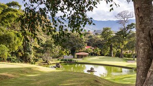 Un campo de golf con un estanque, rodeado de árboles y una montaña al fondo.