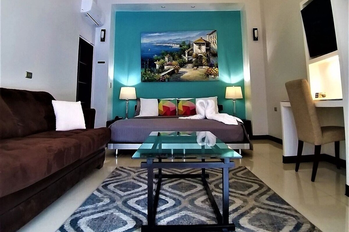 A modern hotel room with a bed, a sofa, a desk, and a painting on the wall.