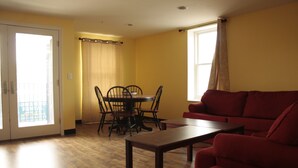En stue med en rød sofa, et træsofabord, et spisebord med stole og en skydedør, der fører ud til en balkon.