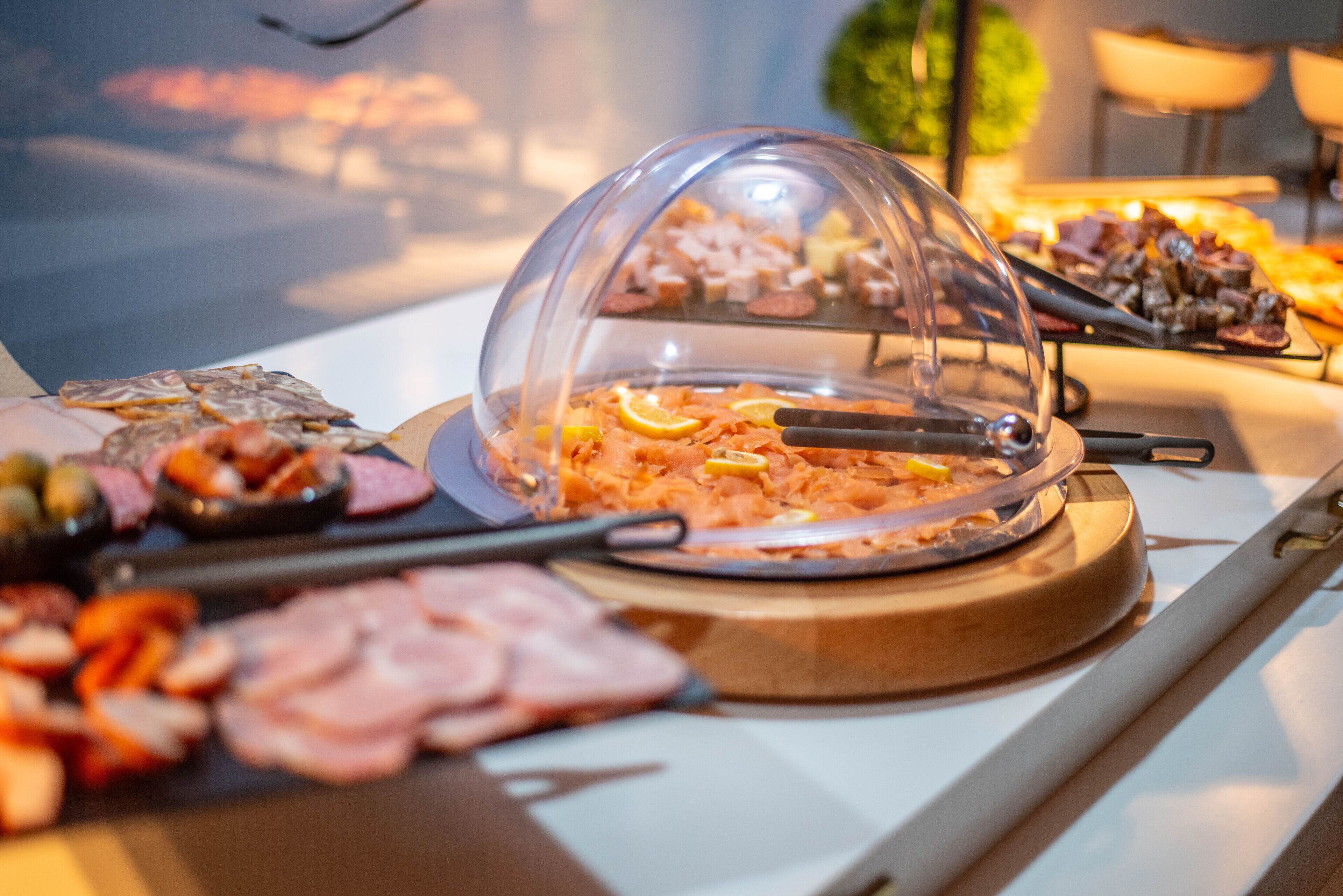 Un bufé con diferentes opciones de comida, incluyendo carnes y quesos, cubiertos por una cúpula.