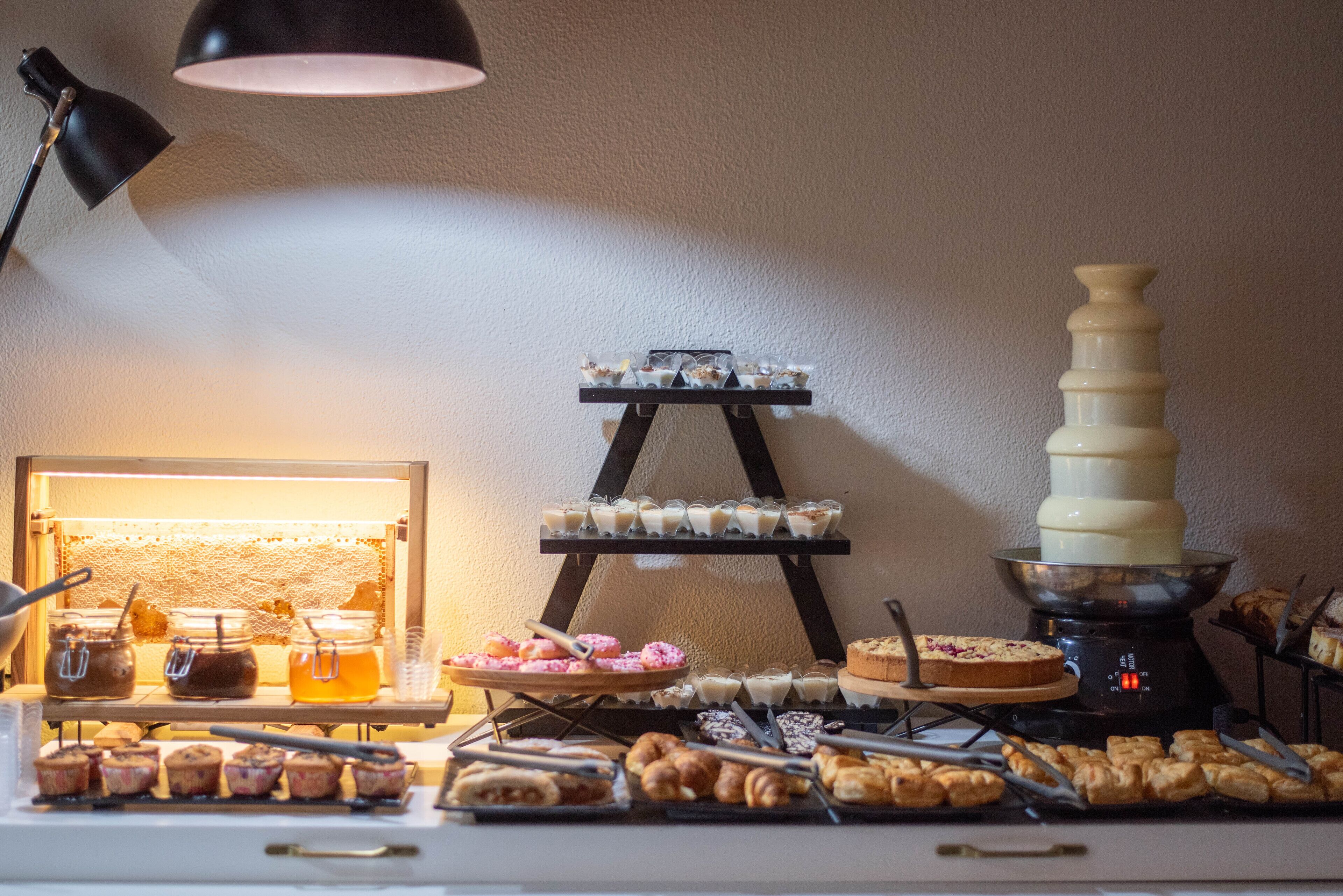 A buffet setup with various food items, a honey dipper, and a chocolate fountain.