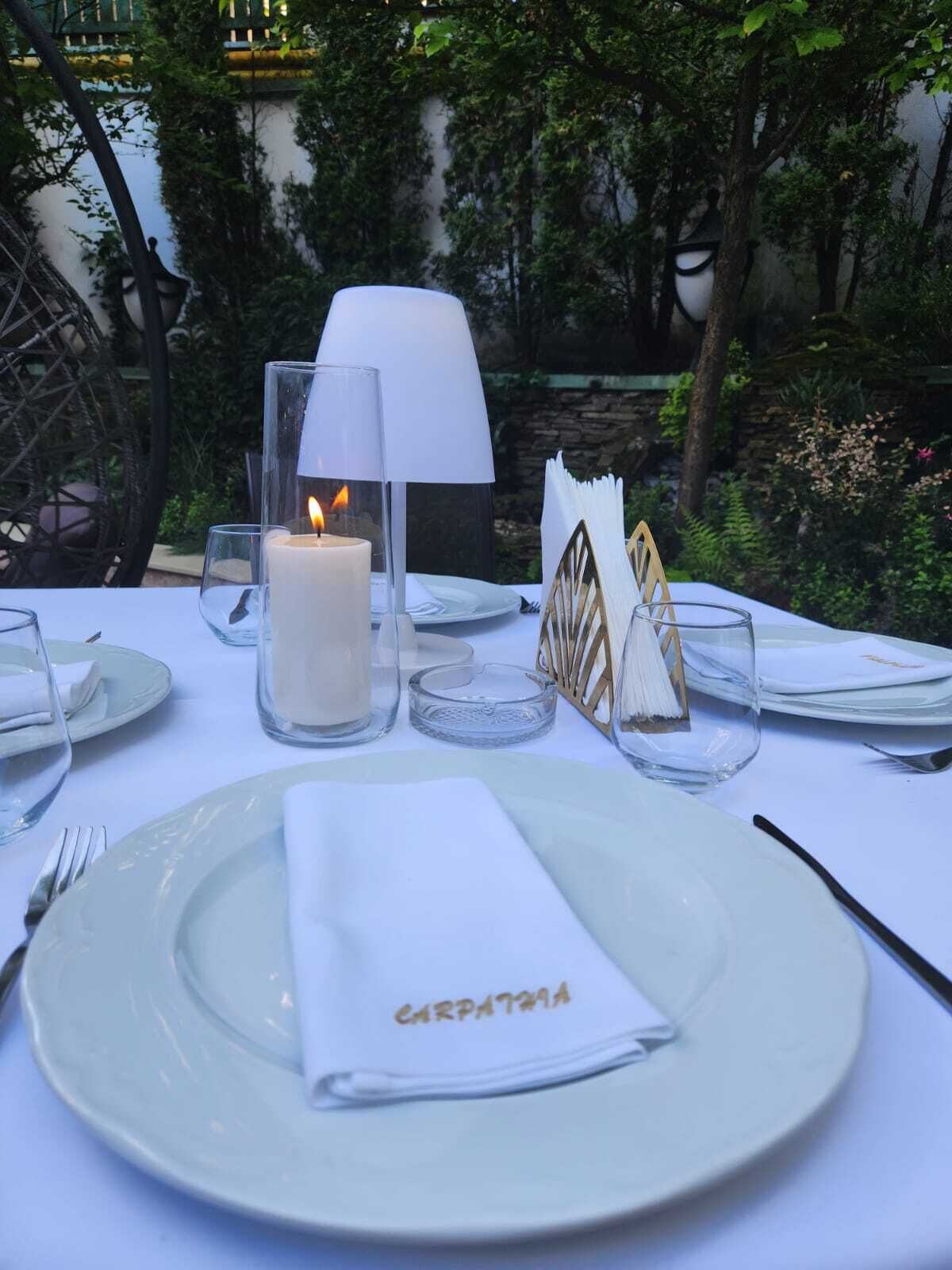 A table set for a meal outdoors with a candle, a lamp, and a napkin with "CARPATTA" written on it.
