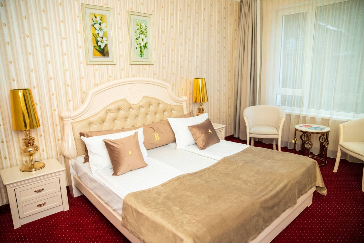 Ein Hotelzimmer mit einem großen Bett, zwei Nachttischlampen, einem Sessel, einem kleinen Tisch und zwei gerahmten Blumenbildern an der Wand.