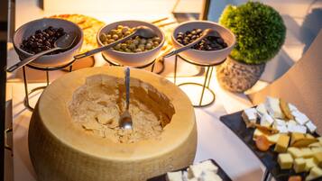 Un bufé con un queso grande en rueda, cuencos de aceitunas y una variedad de quesos y galletas.