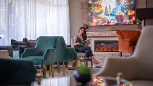 A cozy living room with a fireplace, comfortable seating, and a large TV screen displaying a festive scene. - Hotel Carpathia (Sinaia)