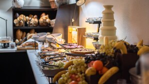 A buffet with various food items, including fruits and pastries, and a lamp in the background. - Hotel Carpathia (Sinaia)