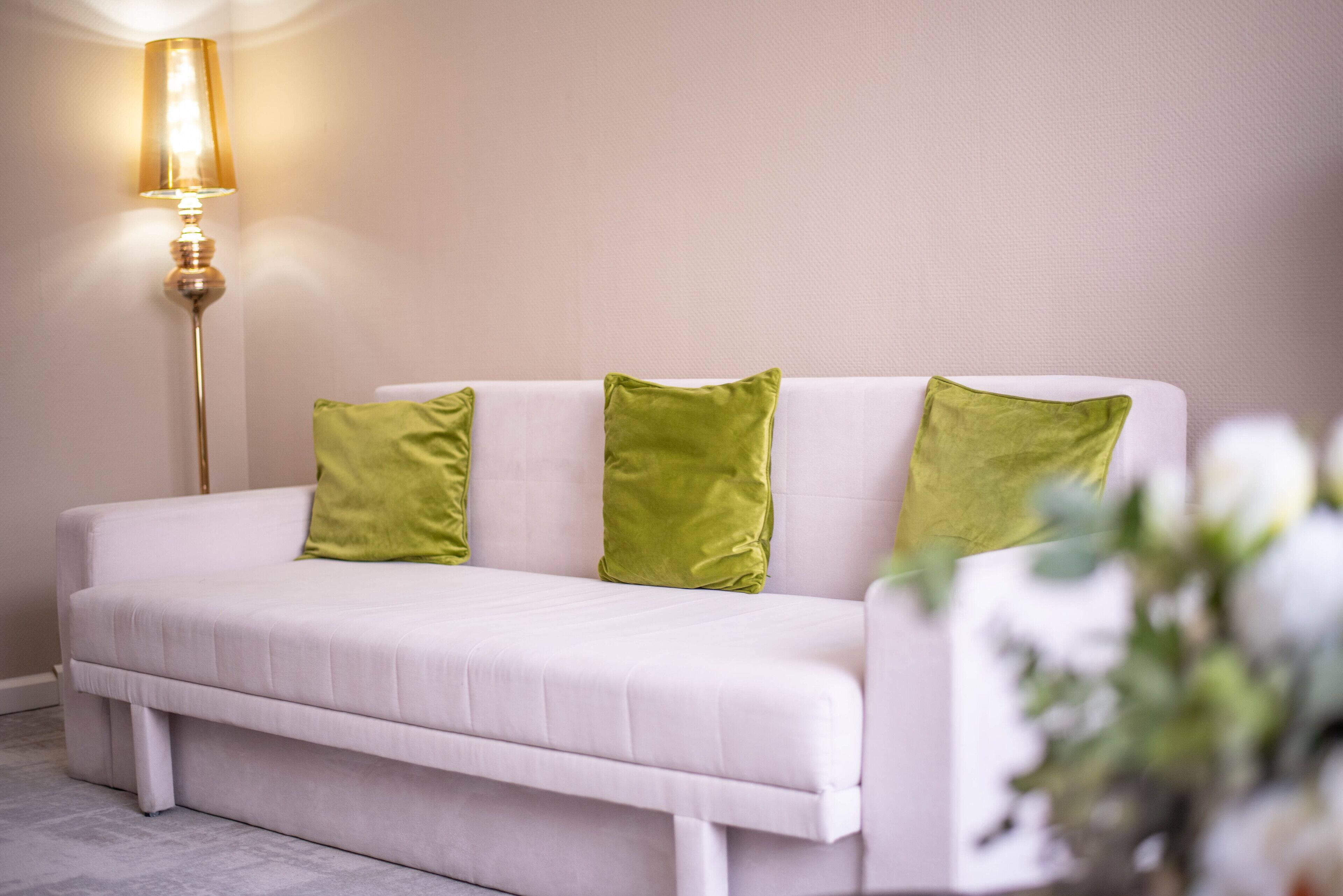 A white sofa with green cushions and a floor lamp.