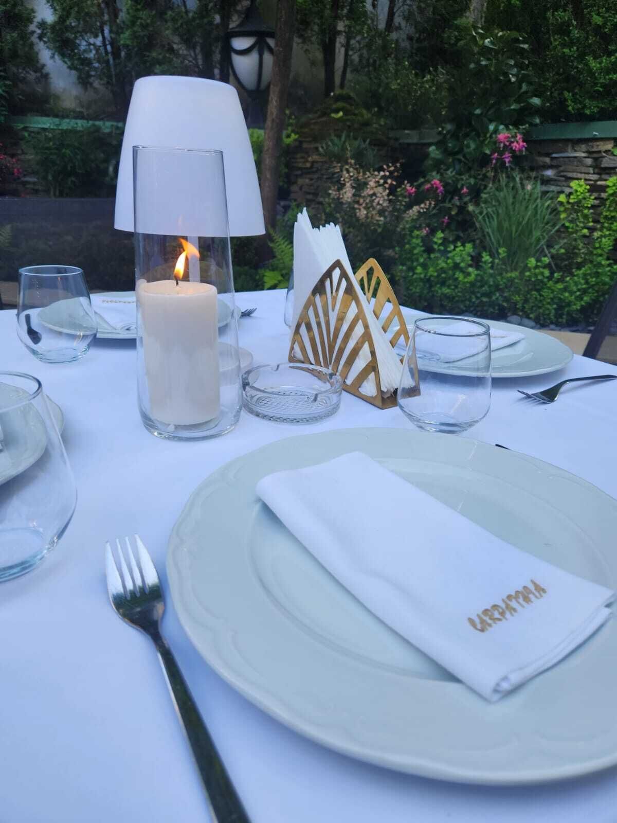 A table set for dining outdoors with a lit candle, clear glasses, and neatly folded napkins.