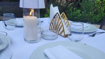 A table set for dining outdoors with a lit candle, clear glasses, and neatly folded napkins.