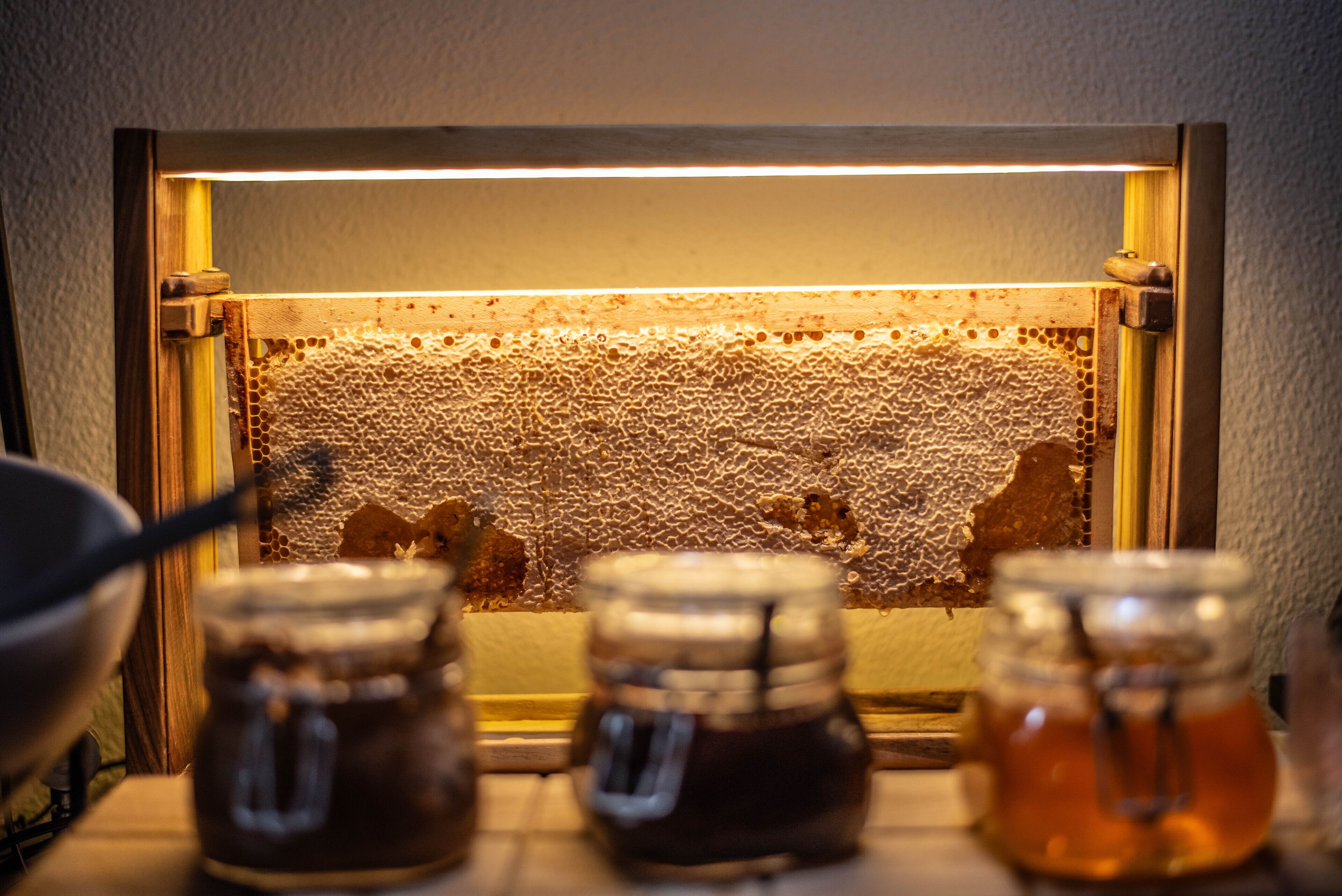 Ein Bienenstockrahmen mit Honiggläsern im Vordergrund.