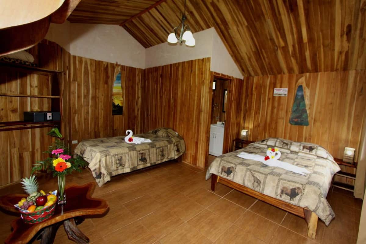 A rustic wooden room with two beds, a wooden ceiling, and a small table with a fruit bowl.
