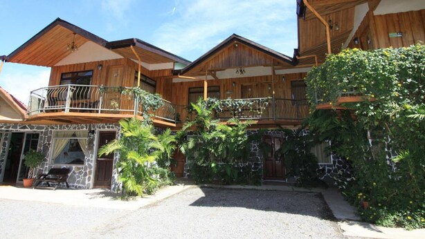 A wooden chalet with a stone facade, multiple balconies, and lush greenery. - Historias Lodge (Monteverde)