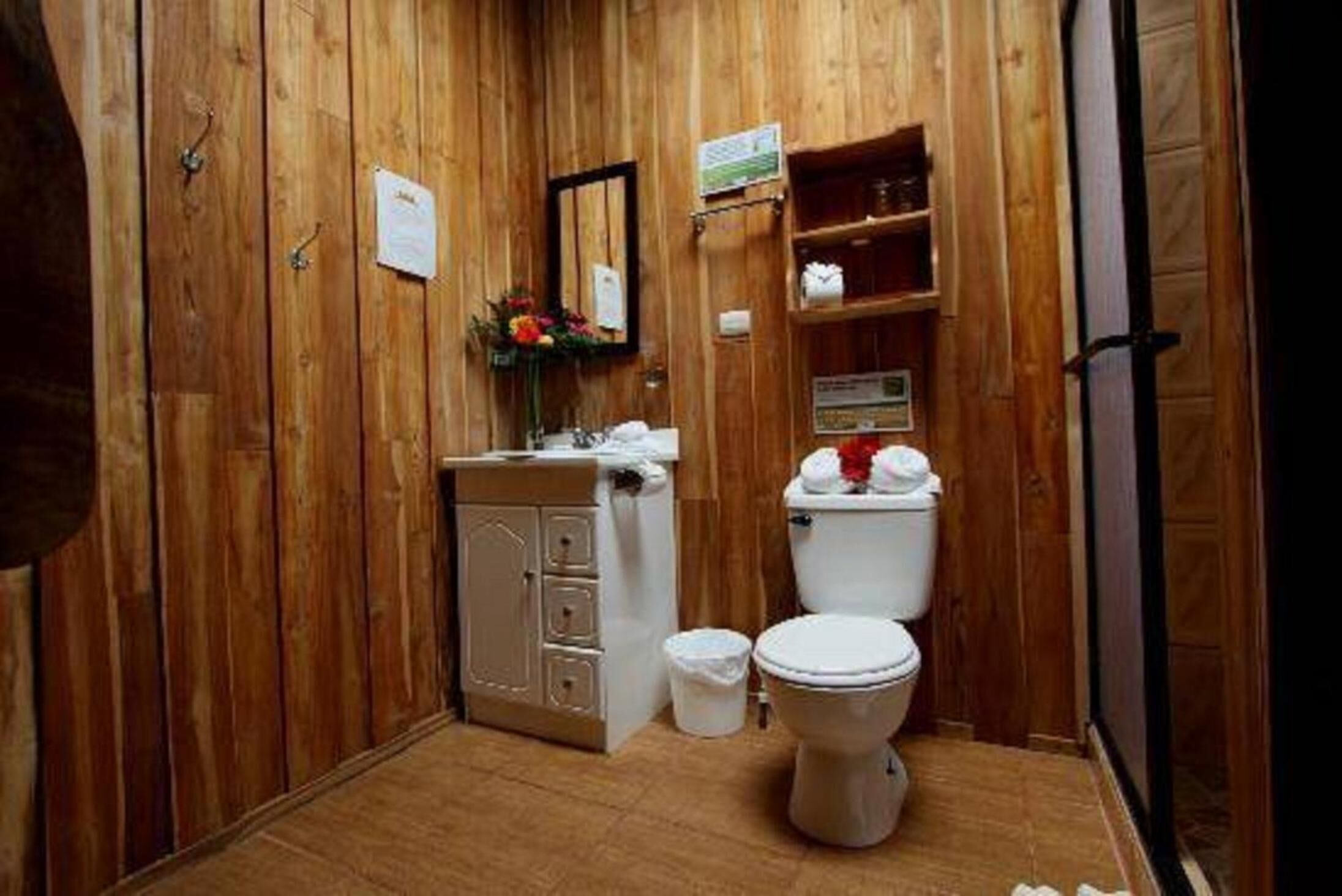 A wooden-paneled bathroom with a toilet, sink, cabinet, and a small trash bin.