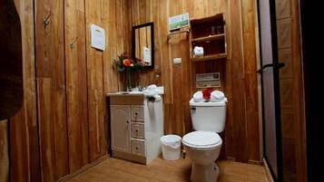 A wooden-paneled bathroom with a toilet, sink, cabinet, and a small trash bin.