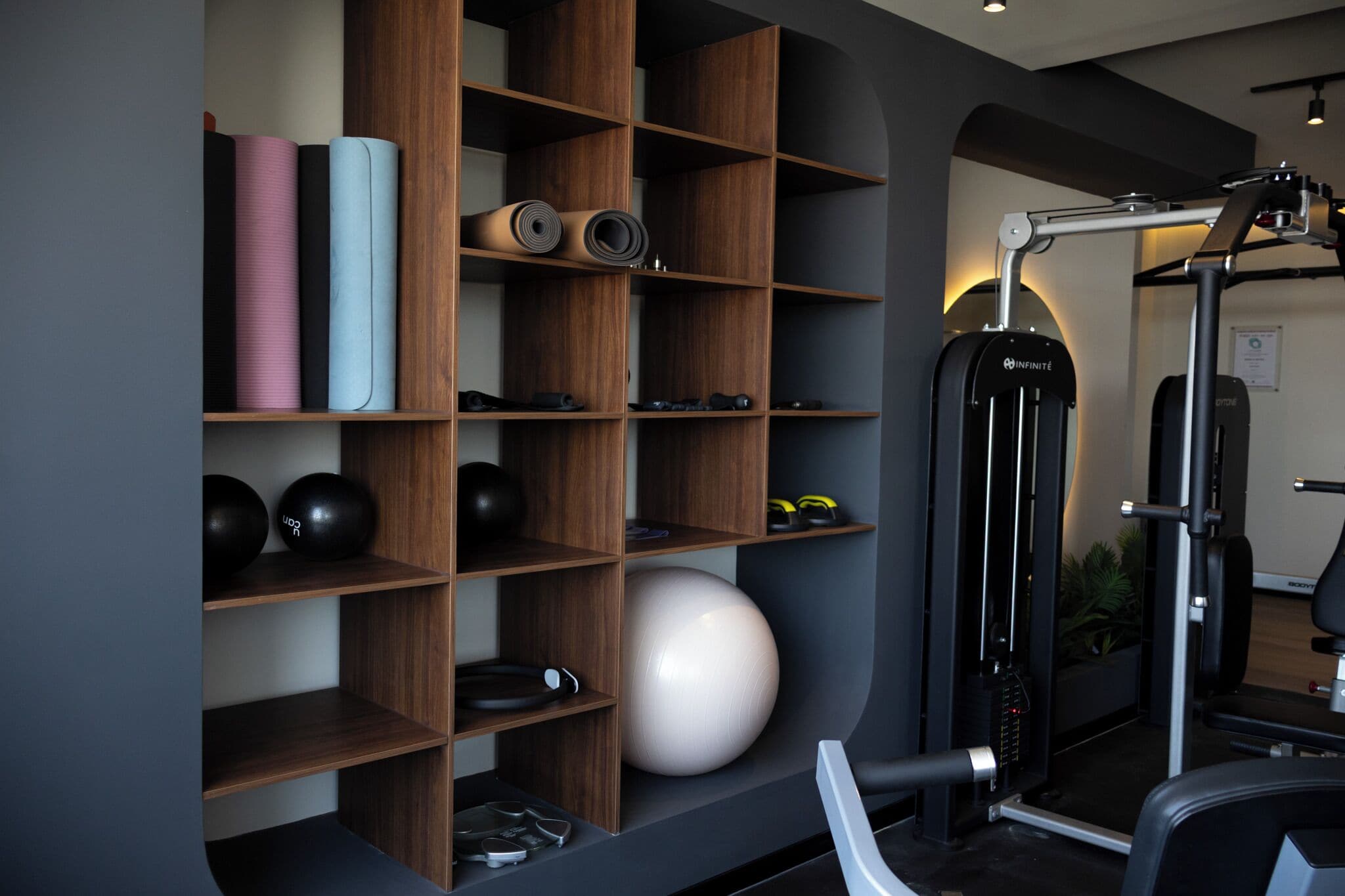 A gym with wooden shelves holding exercise equipment, a large exercise ball, and a wall-mounted machine.