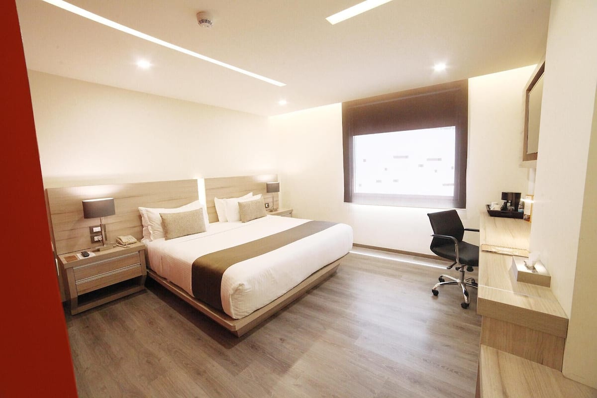 A hotel room with a bed, bedside tables, a desk, a chair, and a window.