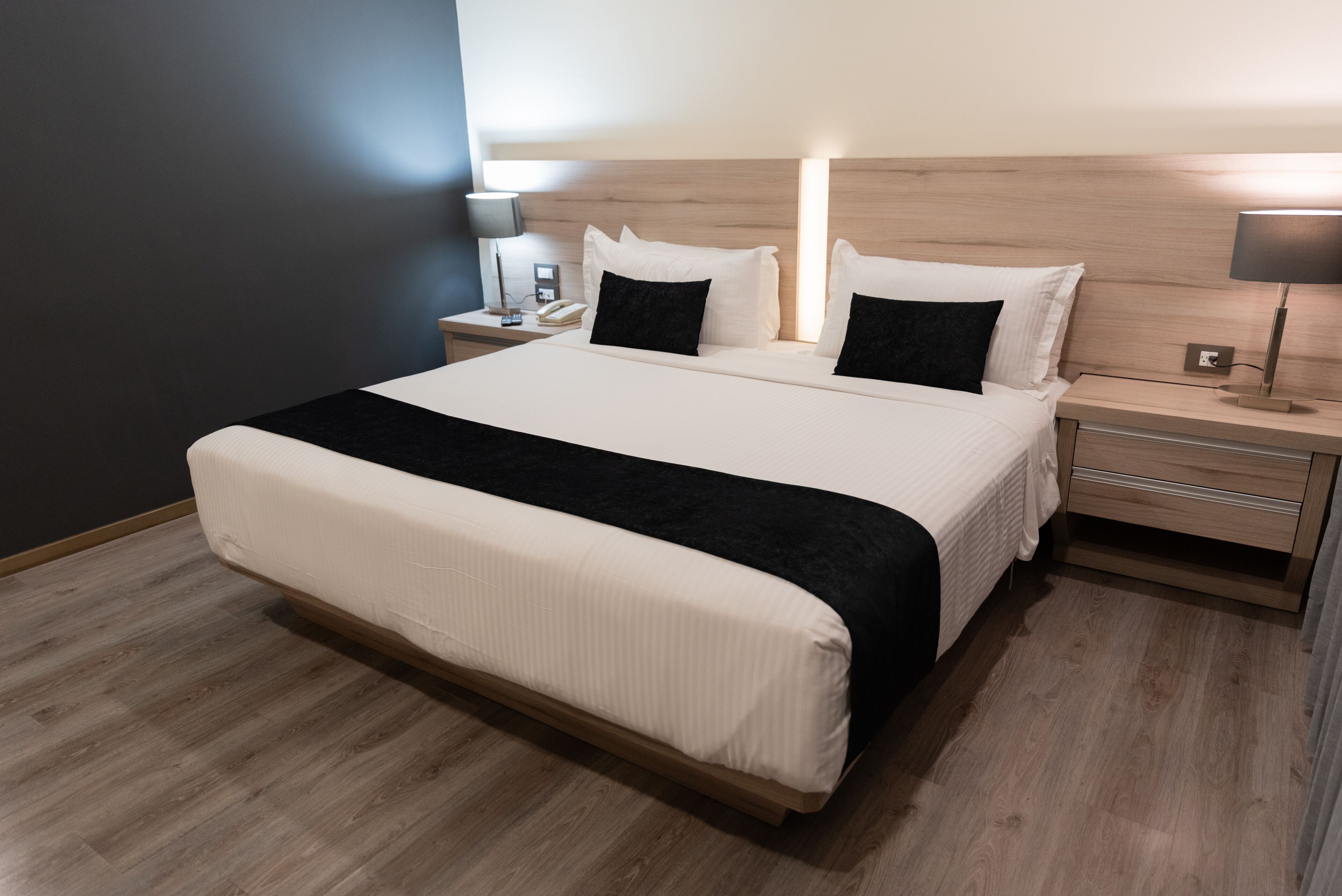 A modern hotel room with a large bed, bedside tables, and a nightstand.