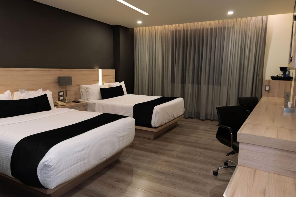 A hotel room with two beds, a desk, a chair, and a large window with curtains.