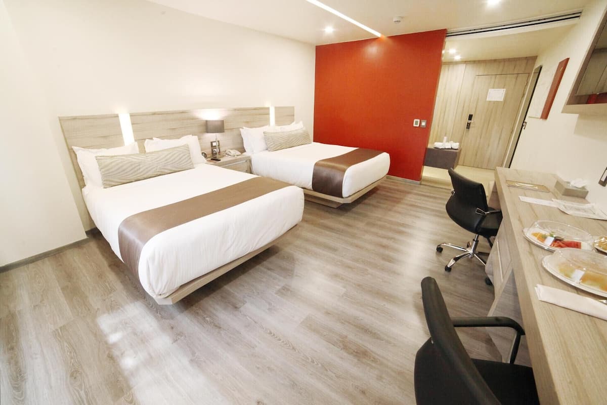 A hotel room with two beds, a desk with a chair, and a red accent wall.