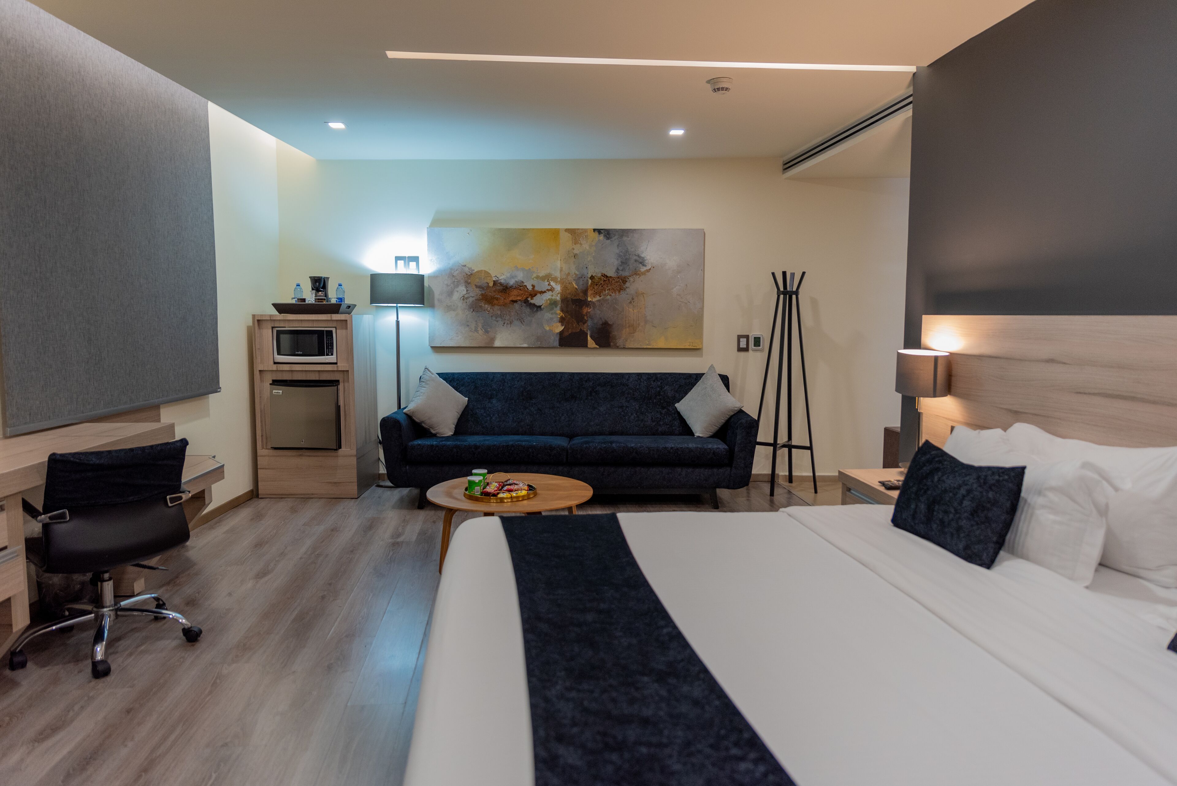 Una habitación de hotel moderna con una cama grande, un escritorio, un sofá, una mesa de centro y un cuadro en la pared.