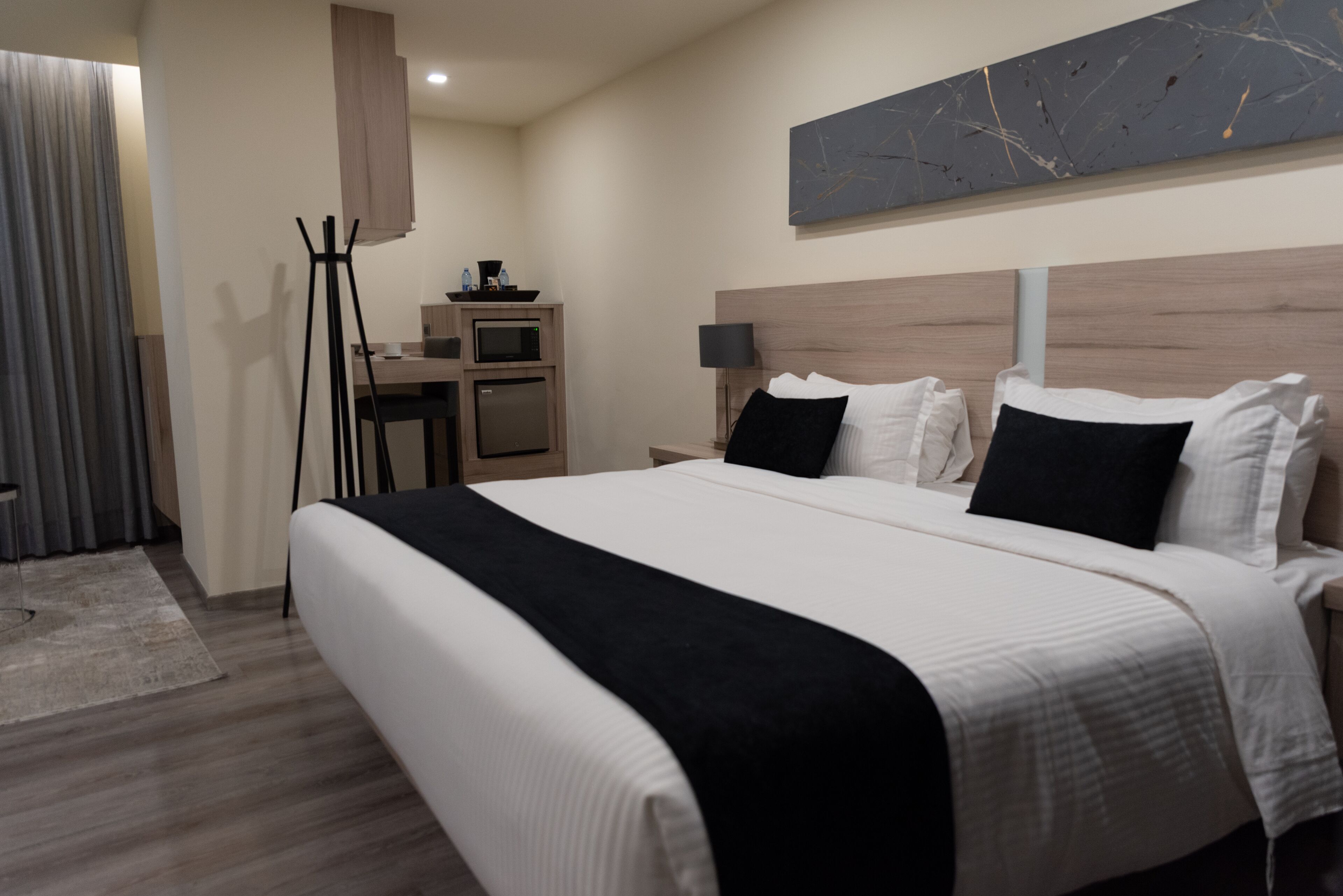Een moderne hotelkamer met een groot bed, een bureau met een computer, een flatscreen televisie en een kleine kitchenette.