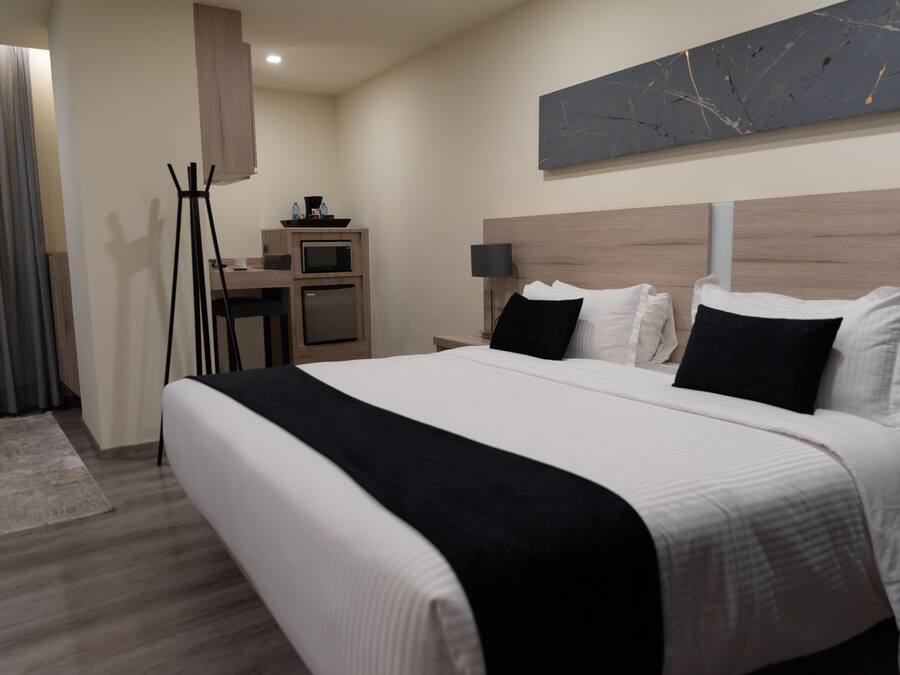 Een moderne hotelkamer met een groot bed, een bureau met een computer, een flatscreen televisie en een kleine kitchenette.