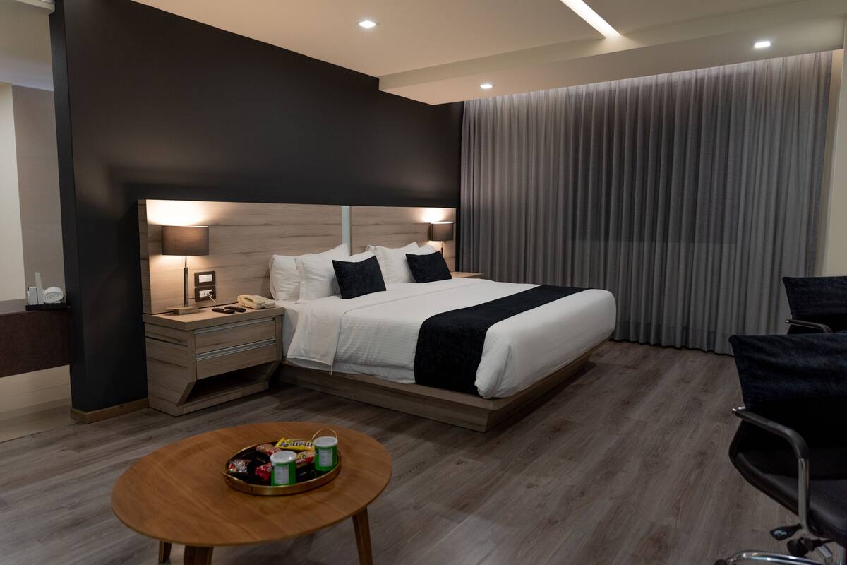 A modern hotel room with a large bed, bedside tables, a desk, and a round table with a tray of items.