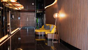 A modern interior with a reflective floor, a curved yellow sofa with grey cushions, and a tall floor lamp.