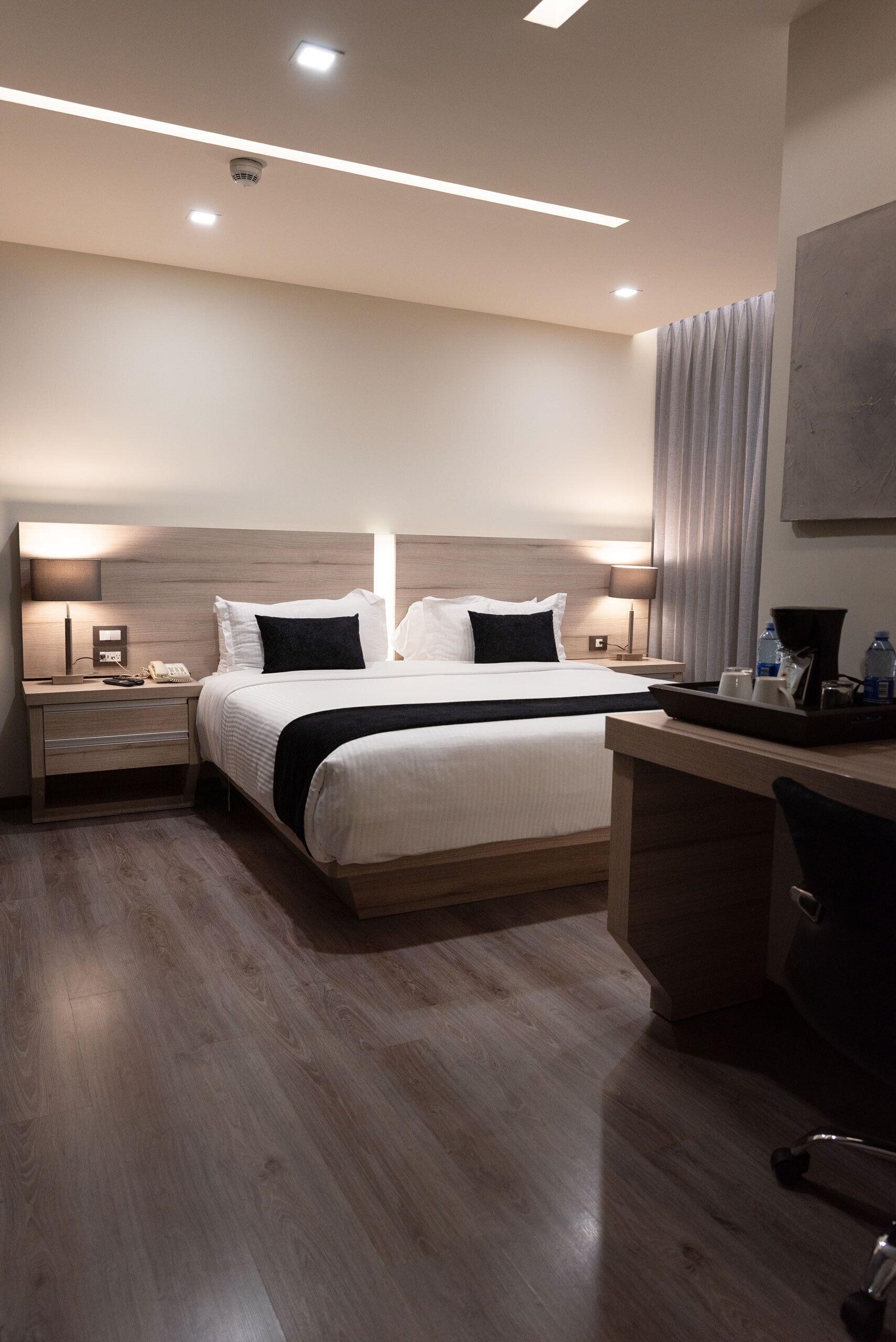 A modern hotel room with a large bed, bedside tables, a desk, and a chair.
