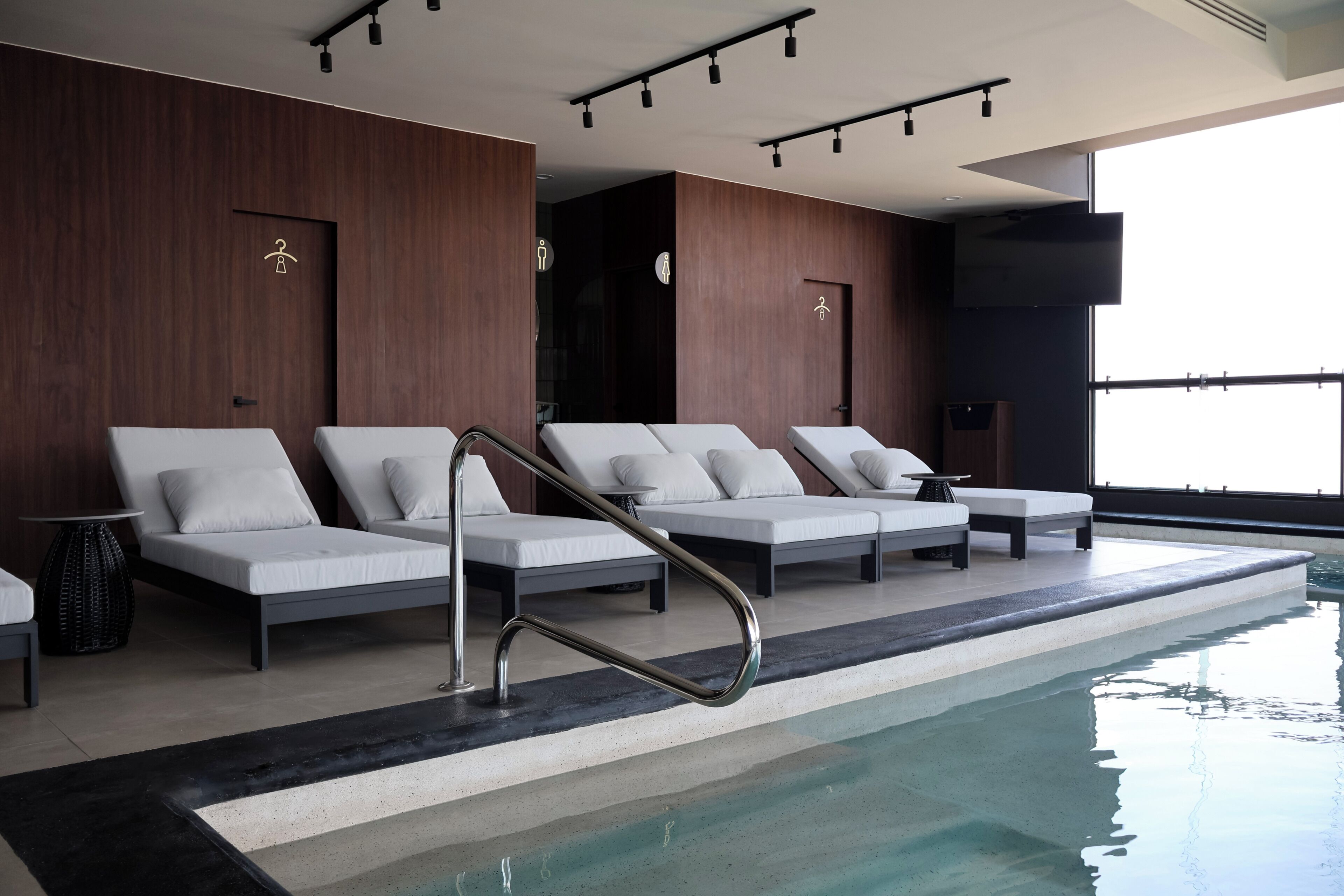 A modern indoor pool area with lounge chairs and a poolside bar.