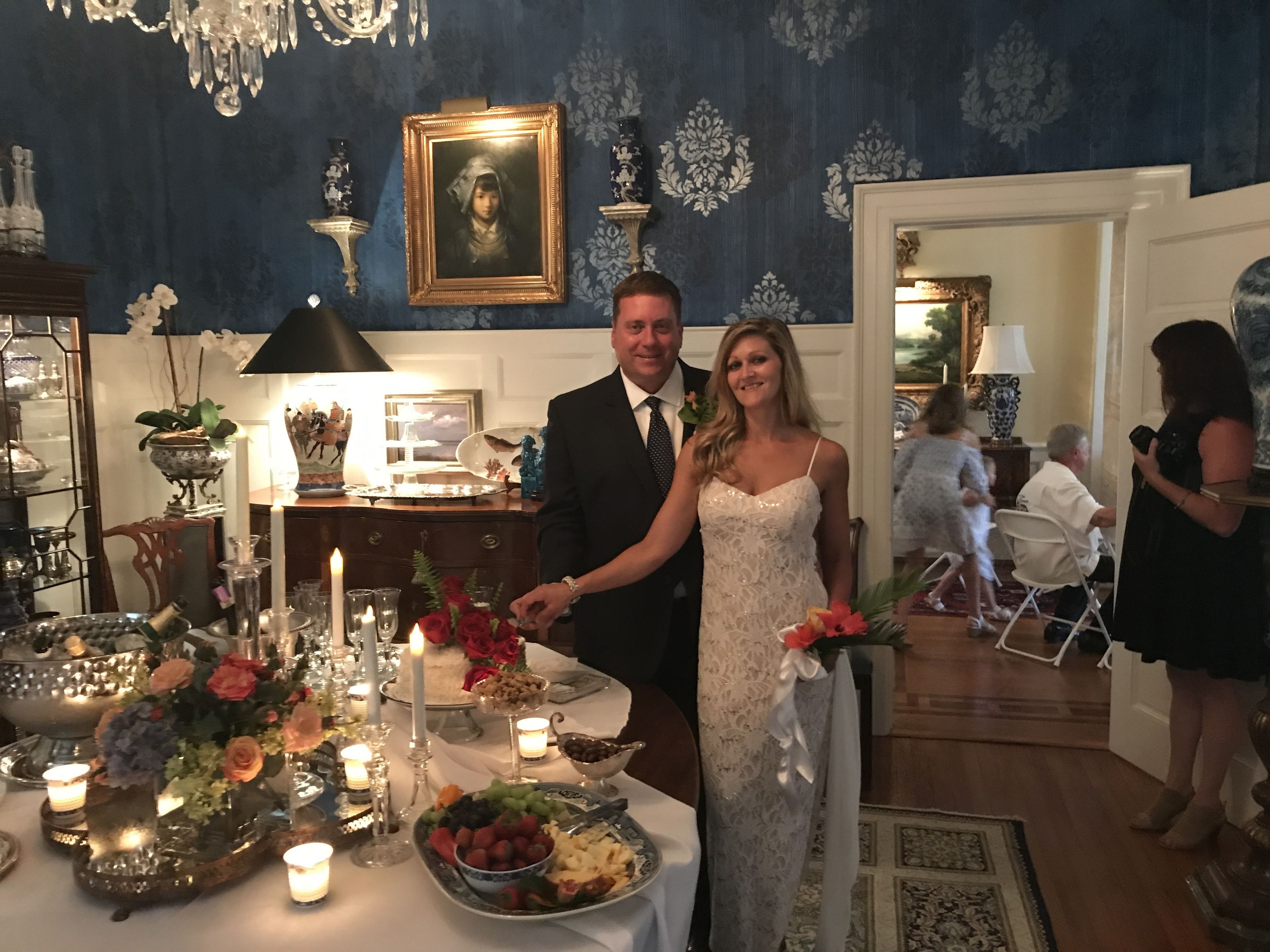 A couple standing at a decorated table with a floral arrangement, candles, and a cake.