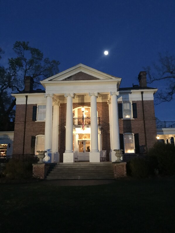 A large, historic building with a central entrance flanked by columns, a brick facade, and a well-lit interior.
