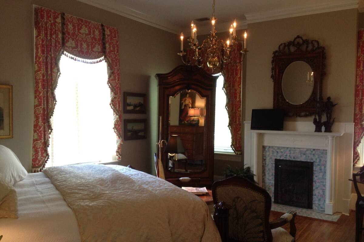 Une chambre à coucher avec un grand lit, un lustre, une cheminée et un miroir.