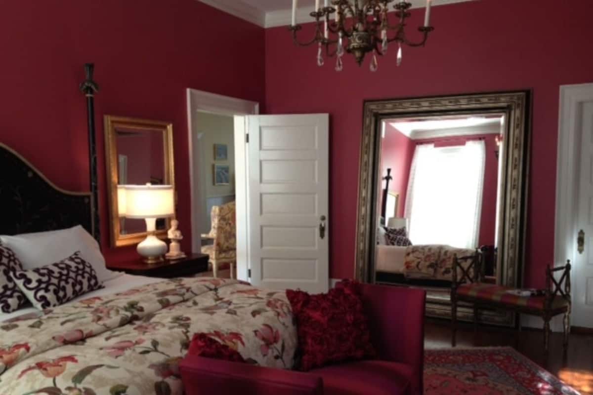 Une chambre à coucher avec un grand lit, une chaise, un miroir et un lustre.