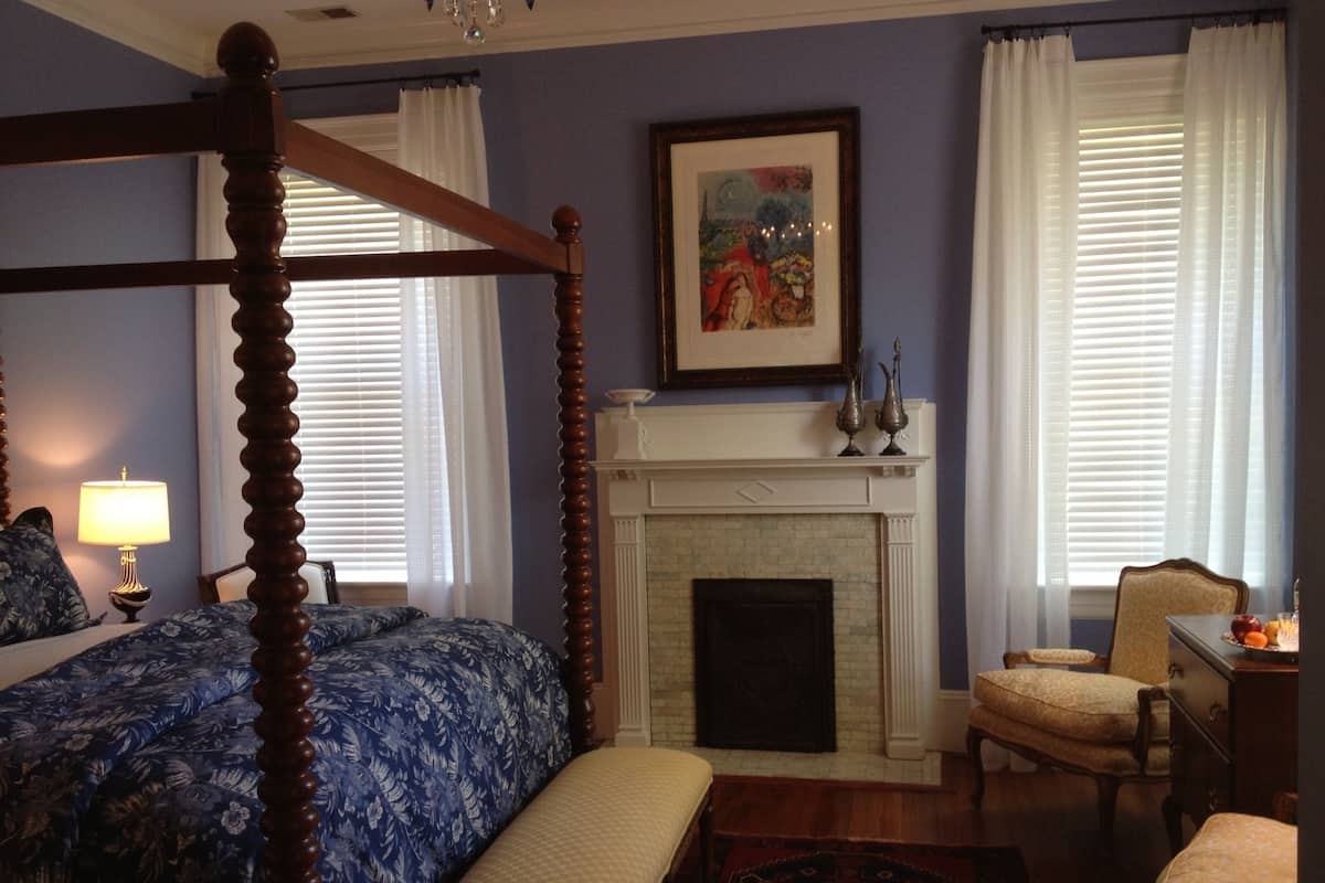 Une chambre à coucher avec un lit à baldaquin, une cheminée et un fauteuil.