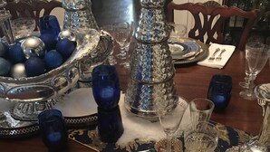 Une table à manger dressée avec des couverts en argent finement ouvragés, de la verrerie bleue et des assiettes décoratives.