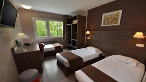 Habitación de hotel con dos camas, un escritorio, una silla, un cesto de basura y una ventana con vista a árboles.