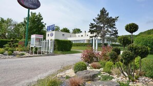 A hotel entrance with a sign, a reception desk, and a well-maintained garden. - Hôtel Val Vert (Creancey)