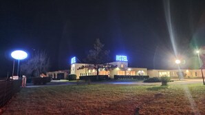 Un hotel con un llamativo letrero que dice 'HOTEL', una entrada bien iluminada y un área de estacionamiento.
