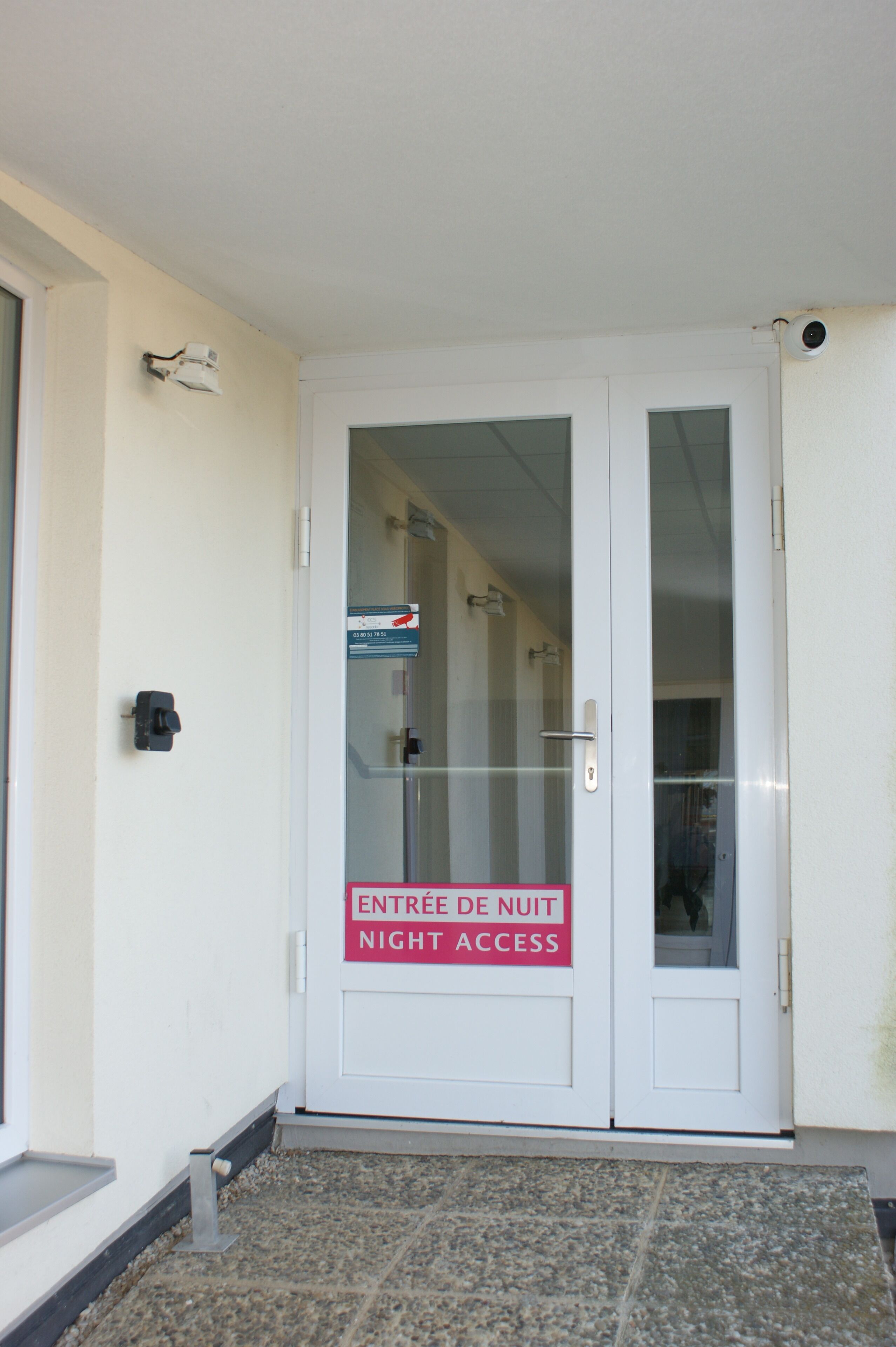 En vit dörr med en skylt som visar texten ”ENTREE DE NUIT NIGHT ACCESS” och ett titthål.