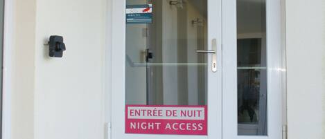 En vit dörr med en skylt som visar texten ”ENTREE DE NUIT NIGHT ACCESS” och ett titthål.