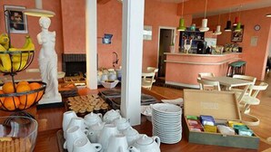 Un bufé de desayuno con teteras blancas, platos y un bol de fruta.