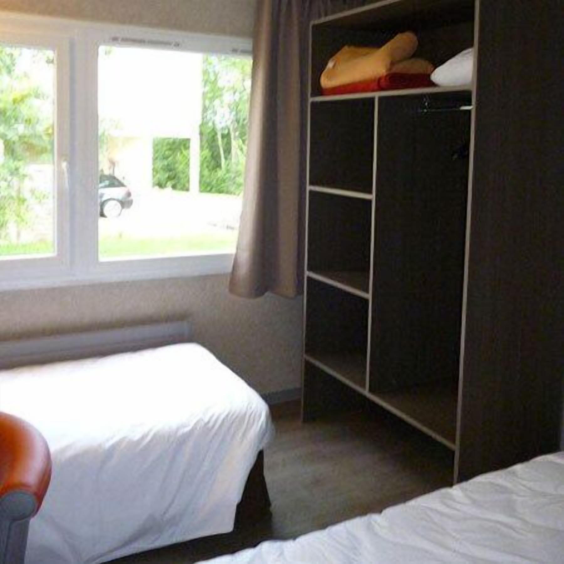Un dormitorio con cama, armario y ventana que ofrece vistas a un coche y vegetación exterior.