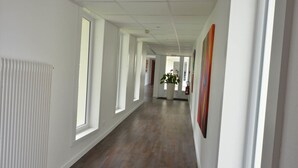 A long, narrow hallway with white walls, wooden flooring, and large windows on one side. - Hôtel Val Vert (Creancey)
