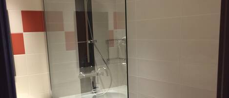 A modern bathroom with a glass-enclosed shower, a white sink, and a black and white tiled wall.