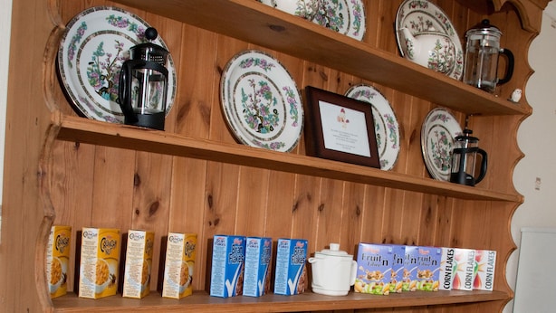 Um armário de madeira com prateleiras contendo pratos, cafeteira, bule e caixas de cereal.