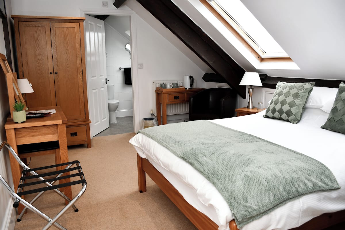 Un dormitorio con cama, escritorio, silla, armario y tragaluz.