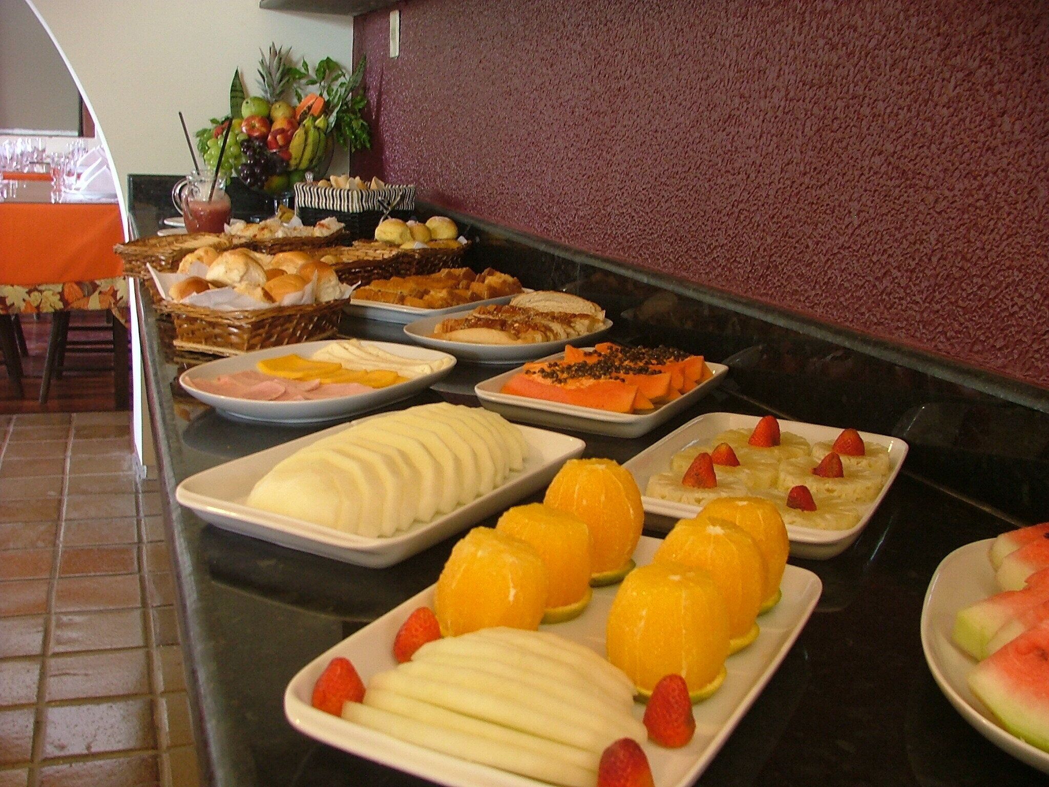 Buffet com diversos alimentos, incluindo frutas, doces e salada de frutas.