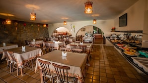 A restaurant with multiple dining tables and chairs, a buffet area, and hanging light fixtures.