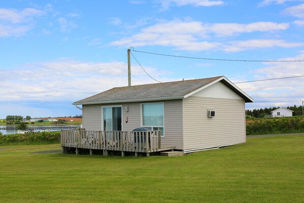 A small, single-story cabin with a wooden deck, a large window, and a door.